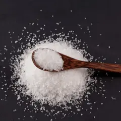 Drewniana łyżka z kryształkami soli na czarnym tle. To msg, które dodaje smaku potrawom.