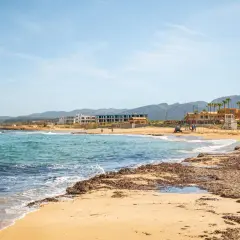 Piękne, turkusowe morze na Krecie, z piaszczystą plażą i hotelami w tle.
