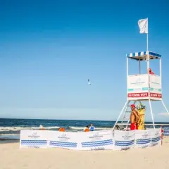 Biała flaga nad morzem oznacza bezpieczną kąpiel. Ratownik czuwa z wieży ratowniczej na plaży.