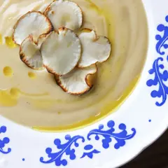 Aksamitny zupa krem z topinamburu, udekorowana chrupiącymi chipsami z topinamburu i skropiona oliwą.