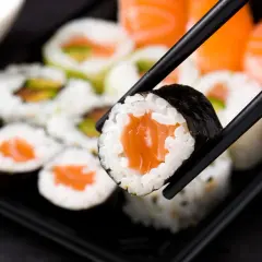Chopsticks trzymają kawałek sushi z łososiem. Czy sushi jest zdrowe? Tak, jeśli wybierasz świeże składniki i umiarkowane porcje ryżu.