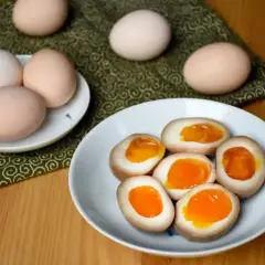 Na talerzu jajka do ramenu z płynnym, pomarańczowym żółtkiem. Obok surowe jajka.