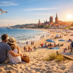 Para zakochanych na plaży, w tle tętniąca życiem linia brzegowa Bałtyku z Gdańskiem i latarnią morską.