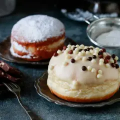 Dwa pączki: jeden oprószony cukrem pudrem, drugi polany lukrem i posypany kuleczkami. Pyszna pokusa, choć pączek kcal może przyprawić o zawrót głowy.