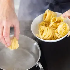 Ręka wkłada porcję tagliatelle do wrzącej wody. Czy makaron gotujemy pod przykryciem? Zobacz, jak zacząć gotowanie.