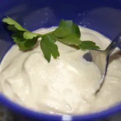 Kremowy sos z tahini, udekorowany gałązką pietruszki, czeka na łyżce w niebieskiej miseczce.