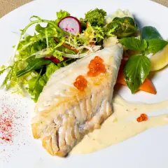 Filet morszczuka z ikrą, podany z sałatką, warzywami i sosem. Czy morszczuk jest zdrowy? Tak, to chuda ryba bogata w białko.