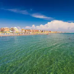 Słoneczny dzień nad morzem w Rzymie. Tłumy ludzi na plaży, kolorowe parasole i budynki w tle.