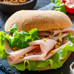 Pyszna kanapka z mortadelą, chrupiącą sałatą i pistacjami na ciemnym tle.