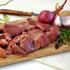 Surowe kawałki wątróbki na desce, obok cebuli, rozmarynu i pieprzu. Czy wątróbka to mięso? Tak, to organ mięśniowy.