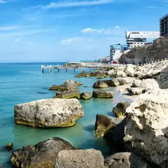 Brzeg największego morza w Europie, z turkusową wodą, kamienistą plażą i nowoczesnymi budynkami na klifie.