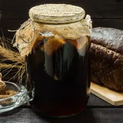 Słoik z ciemnym napojem, obok bochenek chleba i kłosy. Czy kwas chlebowy zawiera alkohol?