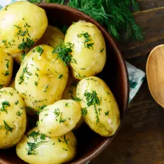 Miska pełna aromatycznych, gotowanych ziemniaków posypanych świeżym koperkiem, obok drewniana łyżka.