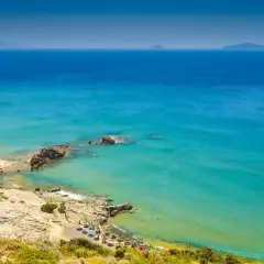 Malownicza zatoka na wyspie Kos, z turkusową wodą, skalistymi klifami i plażą z leżakami.