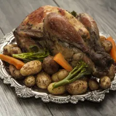 Pieczona perliczka z ziemniakami, marchewką i brokułami na ozdobnej tacy.