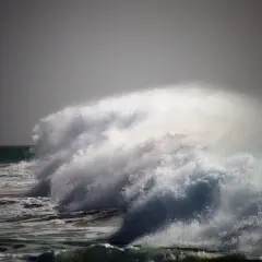 Potężna fala rozbija się na tle burzowego nieba. Woda w **oceanie atlantyckim** jest wzburzona, tworząc kaskady piany i bryzgów.