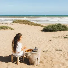 Kobieta pije herbatę na piaszczystej plaży. W tle widać turkusowe morze, które przypomina o pięknie Tunezji.