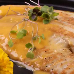 Smażony filet rybny w sosie, udekorowany kiełkami i żółtym kwiatem. Czy amur ma dużo ości? Ten wygląda na bezproblemowy.
