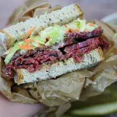 Pyszna kanapka z pastrami, z chrupiącą surówką i ziarnistym pieczywem, zawinięta w papier.