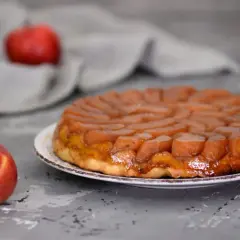 Apetyczna tarta tatin przepis na pyszny deser z karmelizowanymi jabłkami. Obok leży świeże jabłko.