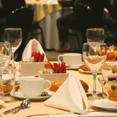 Elegancko nakryty stół w hotelowym lobby, gotowy na śniadanie. Widać owoce, pieczywo, filiżanki i kieliszki.