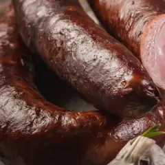 Aromaticzna kiełbasa lisiecka, wędzona i rumiana, z widocznym przekrojem ukazującym soczyste mięso. Obok czosnek i papryczka chili.