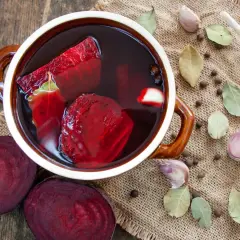 Zakwas z buraków przepis siostry Anastazji w garnku, obok buraki, czosnek, liście laurowe i ziele angielskie.