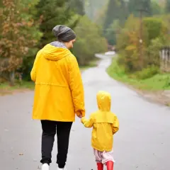 Mama i dziecko w żółtych płaszczach idą za rękę mokrą drogą. Nawet w deszczowe dni Jastarnia oferuje atrakcje, jak spacery po malowniczych okolicach.