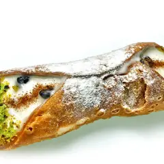 Sycylijskie dania: chrupiąca rurka cannoli z kremem, pistacjami i borówkami, posypana cukrem pudrem.