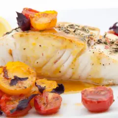 Pyszny halibut ryba pieczony z pomidorkami koktajlowymi i cytryną, polany sosem.