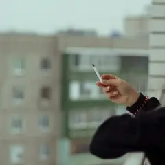 Kobieta z blond włosami pali papierosa na balkonie hotelowym, zastanawiając się, czy można palić na balkonie w hotelu.