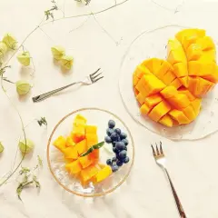 Słodkie mango pokrojone w kostkę, idealne do jedzenia z jagodami i jogurtem. Obok gałązka z zielonymi pąkami.