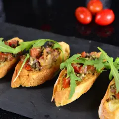 Cztery chrupiące bruschetty z pomidorami i rukolą, idealne jako tapas.