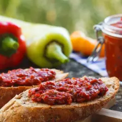 Chleb z pyszną pastą z pieczonej papryki, obok słoiczek i świeże papryki.