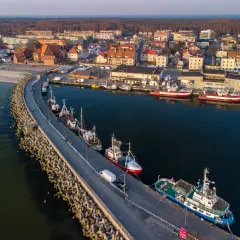 Port w Helu poza sezonem. Spokojne wody, zacumowane kutry i statki, a w tle miasto i las.