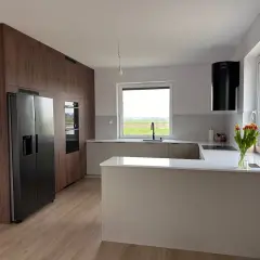 Nowoczesna kuchnia z zabudową w drewnie, wyspą i czarnym okapem. Idealne miejsce na przygotowanie dań haute cuisine.