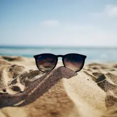 Okulary przeciwsłoneczne na piaszczystej plaży, w tle morze i błękitne niebo. Idealne na wakacje, gdy obowiązuje opłata klimatyczna nad morzem.