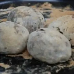 Cztery ziemniaki pieczone w soli, lekko popękane, na czarnej tacy.