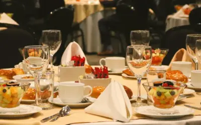 Elegancko nakryty stół w hotelowym lobby, gotowy na śniadanie. Widać owoce, pieczywo, filiżanki i kieliszki.