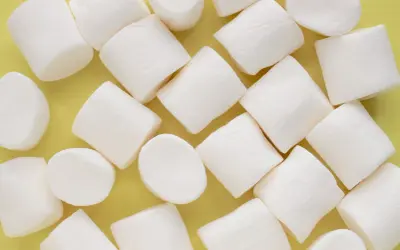 Białe, puszyste pianki marshmallow ułożone na żółtym tle. Pańska skórka, co to za słodka przyjemność!