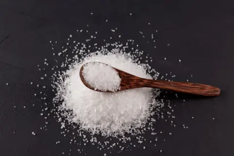 Drewniana łyżka z kryształkami soli na czarnym tle. To msg, które dodaje smaku potrawom.