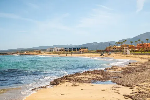Piękne, turkusowe morze na Krecie, z piaszczystą plażą i hotelami w tle.