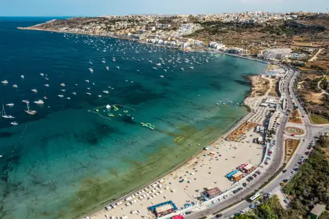 Malta zachwyca turkusowym morzem pełnym łodzi i wodnych atrakcji. Plaże tętnią życiem, a miasto rozciąga się wzdłuż wybrzeża.