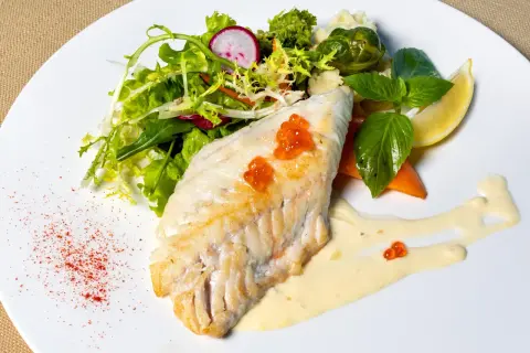 Filet morszczuka z ikrą, podany z sałatką, warzywami i sosem. Czy morszczuk jest zdrowy? Tak, to chuda ryba bogata w białko.