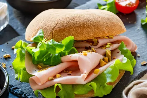 Pyszna kanapka z mortadelą, chrupiącą sałatą i pistacjami na ciemnym tle.