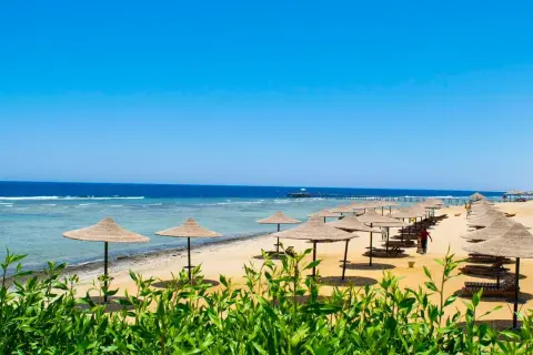 Słoneczny dzień na plaży w kraju nad Morzem Czerwonym. Rzędy parasoli i leżaków czekają na turystów.