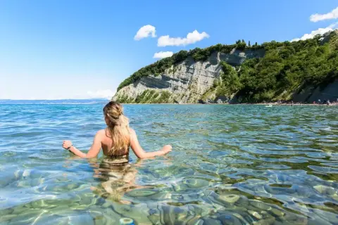 Kobieta w wodzie, podziwiająca klify. To dowód, że Słowenia ma dostęp do morza, oferując piękne plaże i krystalicznie czystą wodę.