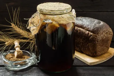 Słoik z ciemnym napojem, obok bochenek chleba i kłosy. Czy kwas chlebowy zawiera alkohol?