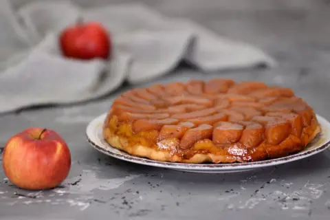 Apetyczna tarta tatin przepis na pyszny deser z karmelizowanymi jabłkami. Obok leży świeże jabłko.