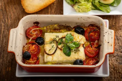 Pyszna pieczona feta z pomidorkami, oliwkami i ziołami w ceramicznym naczyniu. Idealna na lekki posiłek.